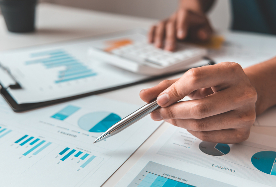 Table filled with paper with graphs and pie charts on as someone uses a calculator