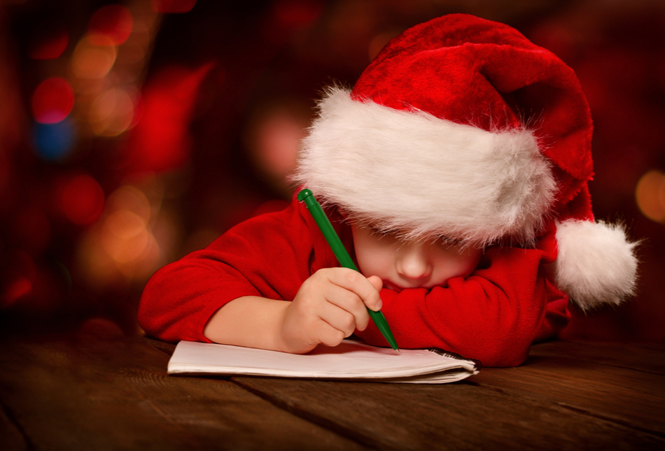 A child writing a Christmas list with a Santa hat on