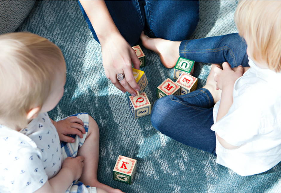 Two young children playing with wooden blocks with their mother