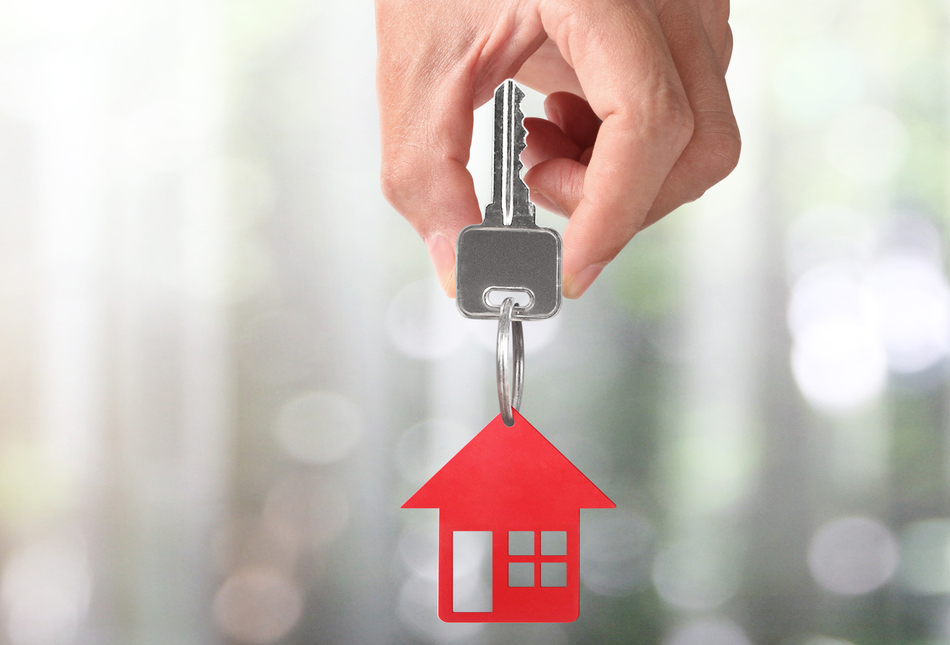 hand holding key with keyring shaped like a house.