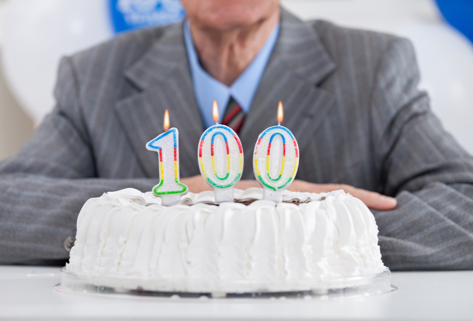 A man sitting behind a cake with “100” birthday candles.