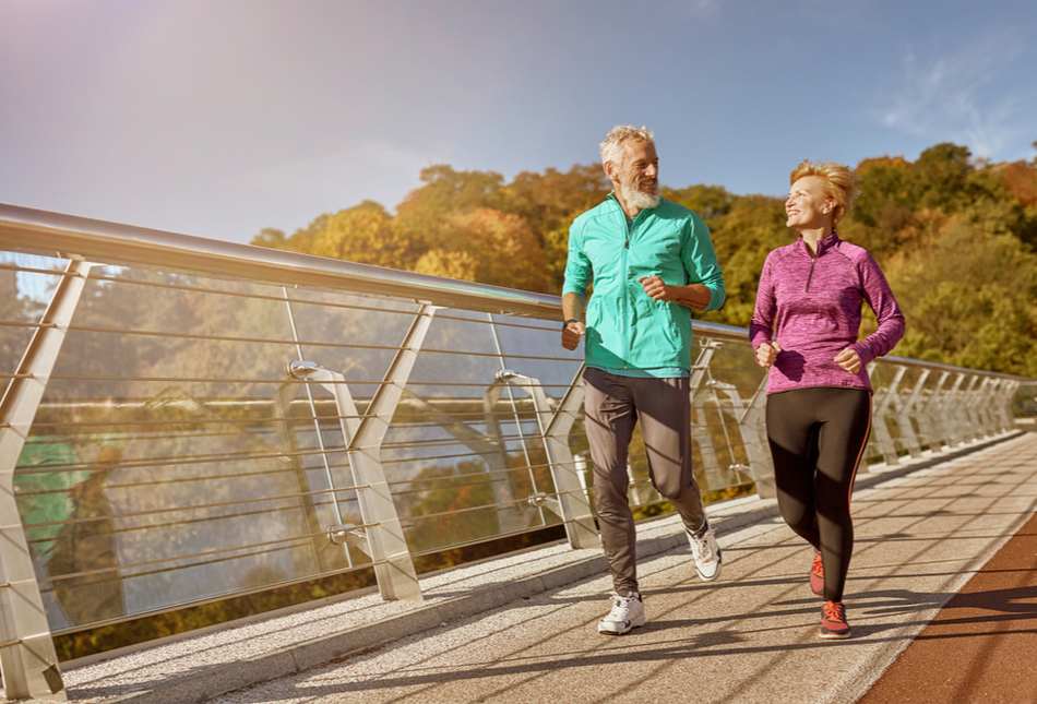 A mature couple jogging across a bridge.