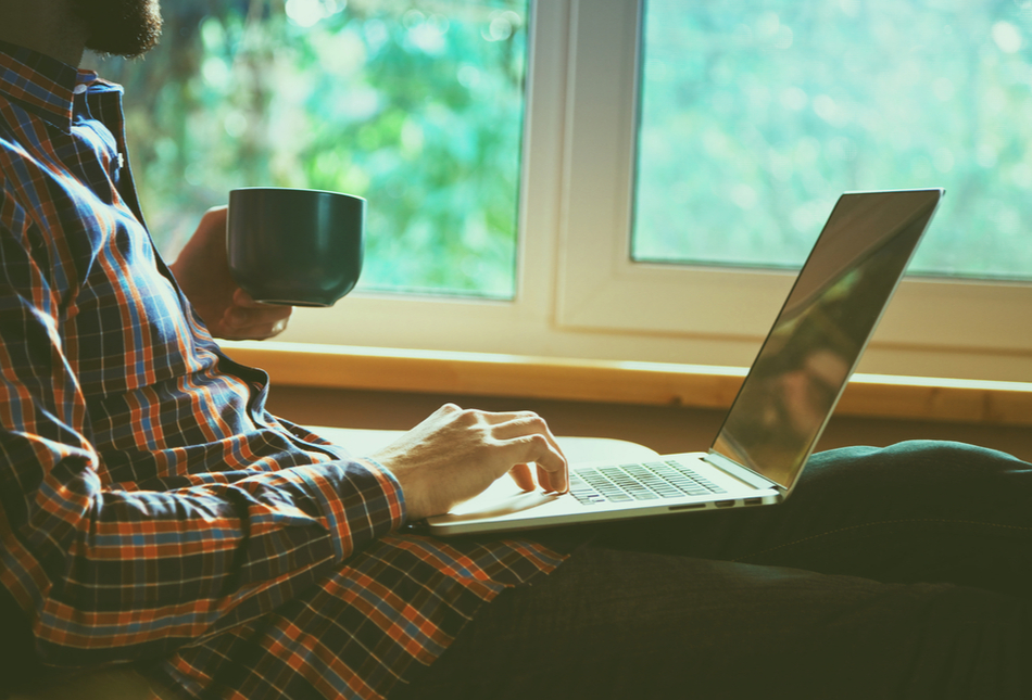 A man using a laptop and drinking a cup of tea.