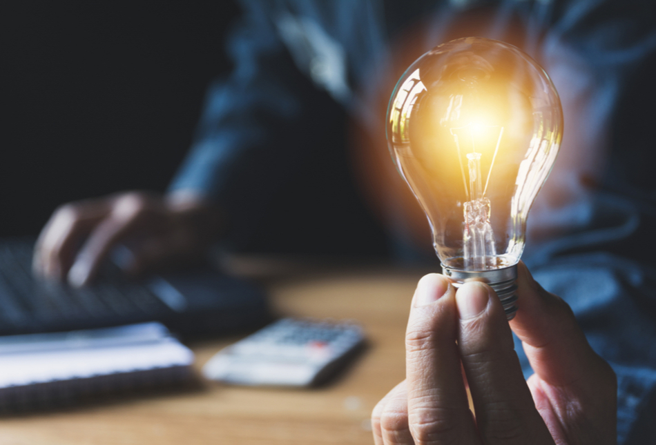 A lit lightbulb with a man using a calculator in the background