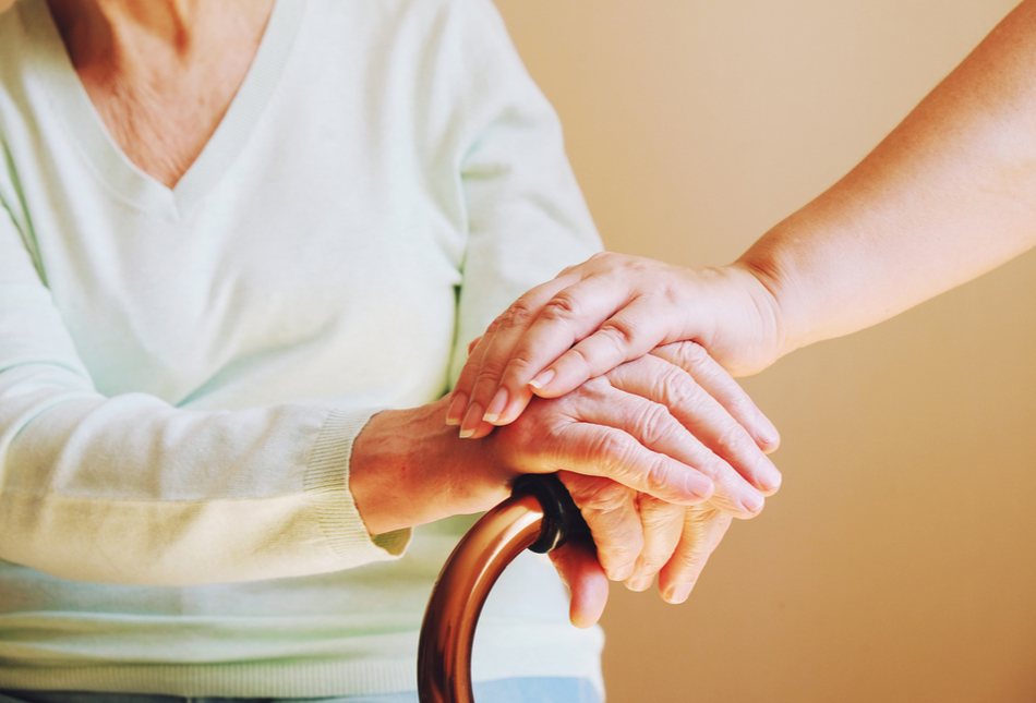 Close-up of someone holding hand the hand of an older woman with a walking aid.