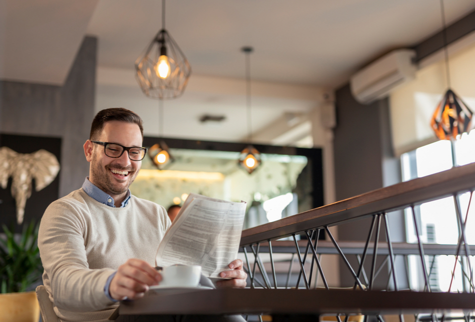 A man reading a newspaper while drinking coffee.