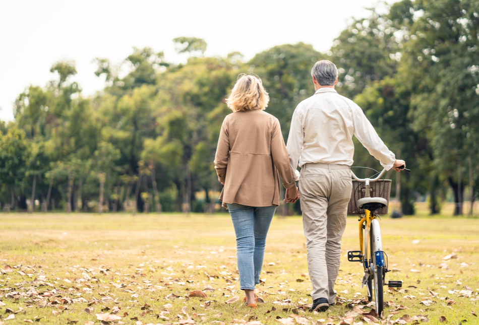 A couple walking through a park and pushing a bike.