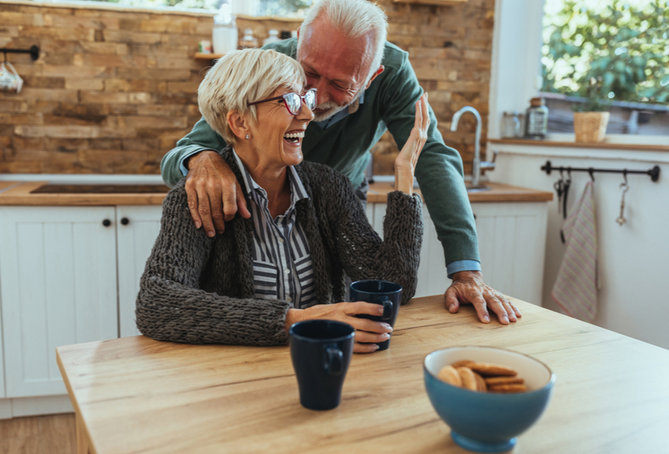 An older couple laughing together in their kitchen.