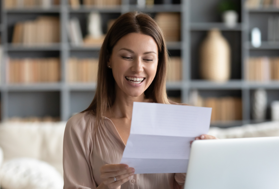 A woman smiling as she reads a letter.
