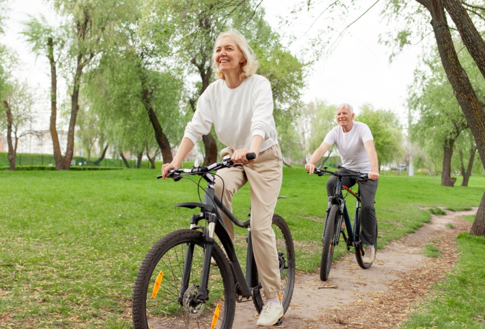 An elderly couple riding their bikes in the park.