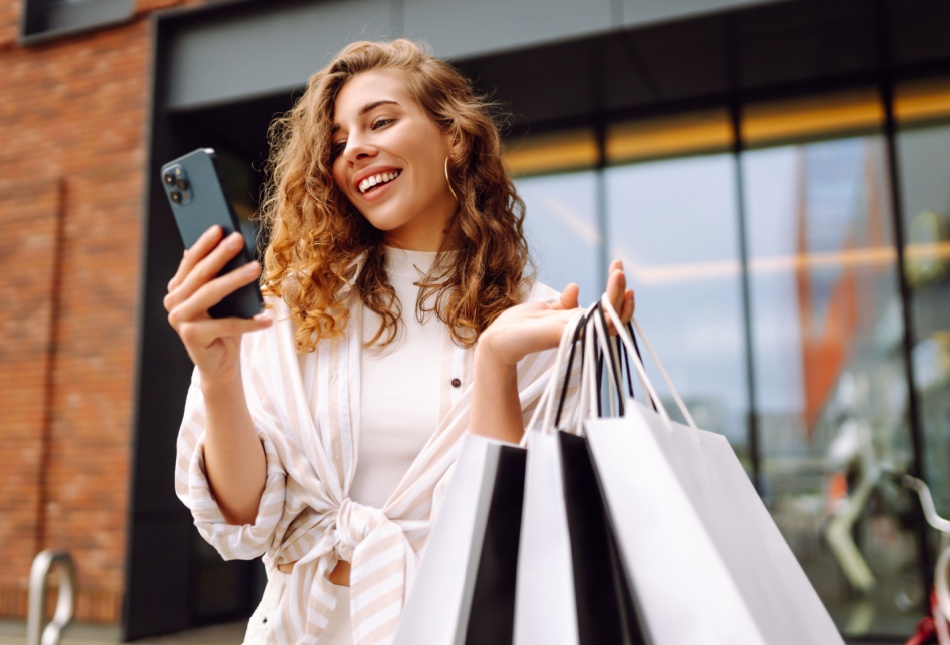 A woman holding shopping bags while on her phone.