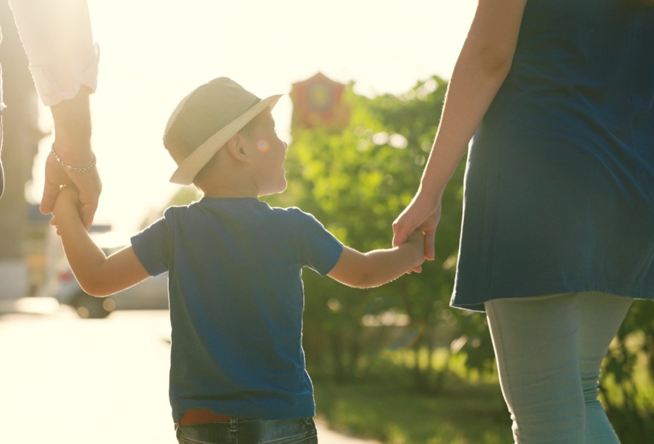 A family with a young child holding hands outdoors.