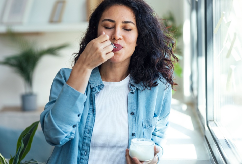 A woman eating a pot of yoghurt.