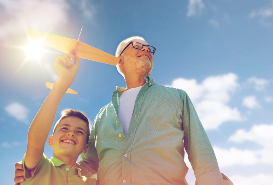 A grandfather and grandson playing with a toy plane outdoors.