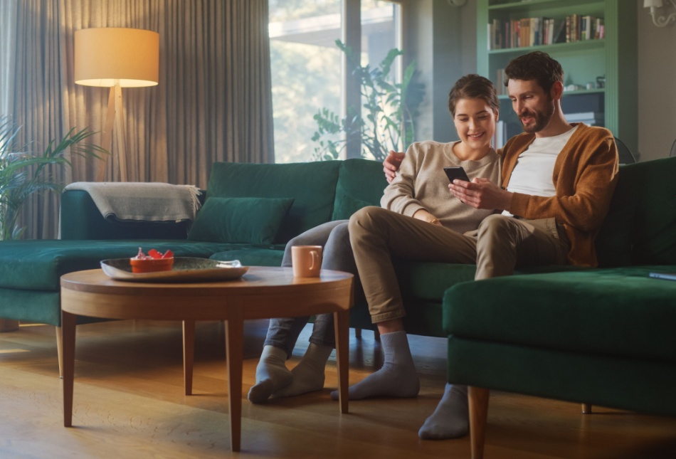 A couple sitting on the sofa together and using a phone.