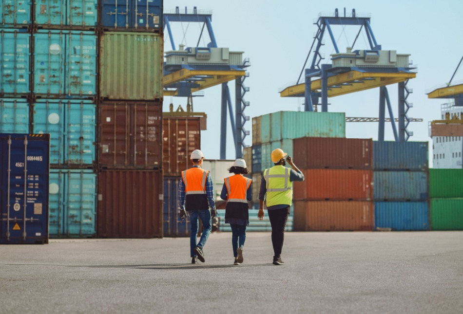 Workers walking through a shipping cargo container terminal depot.