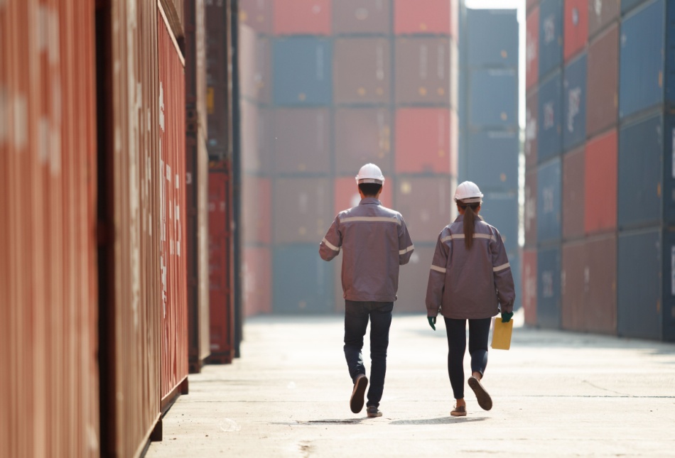 Two workers walking between shopping containers.