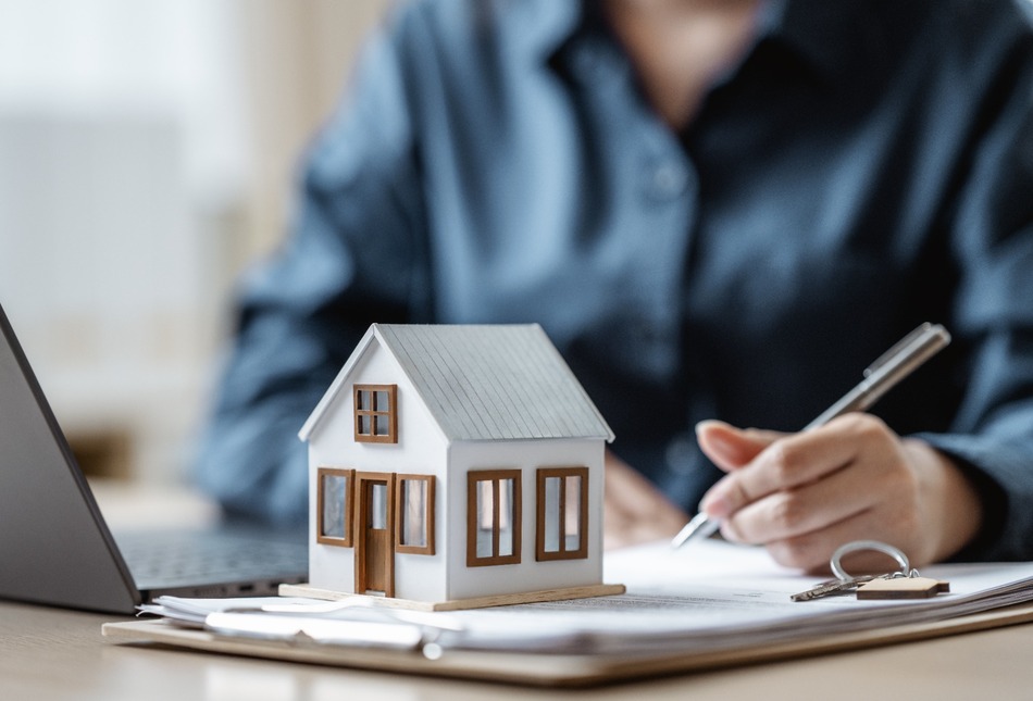 A person signing a document with a model house on the table