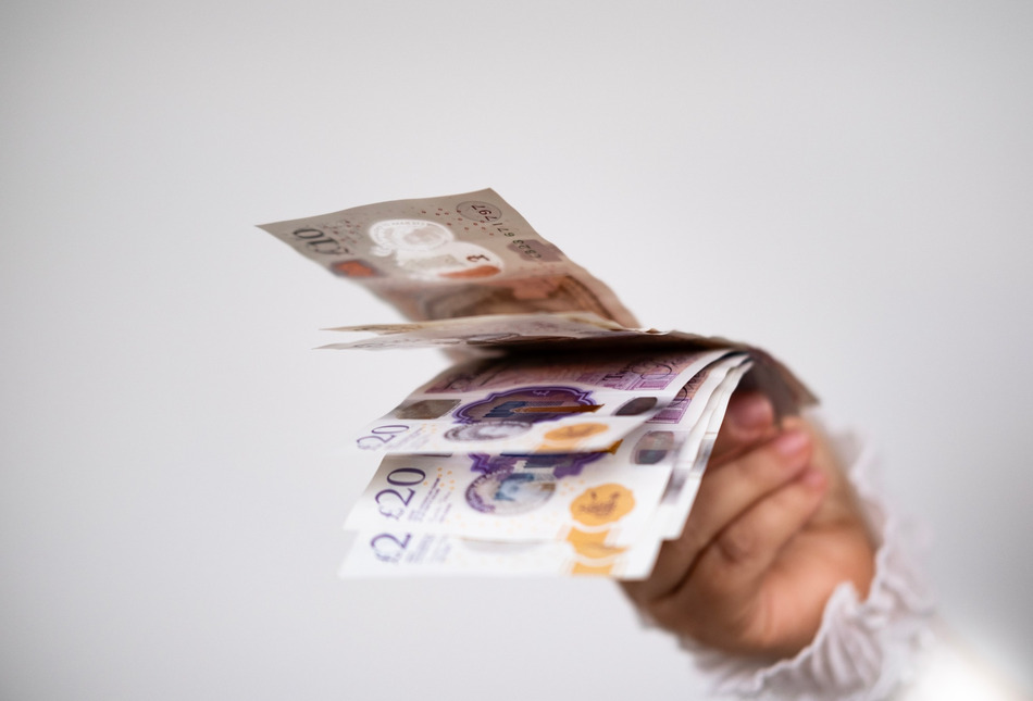 A hand holding UK bank notes.